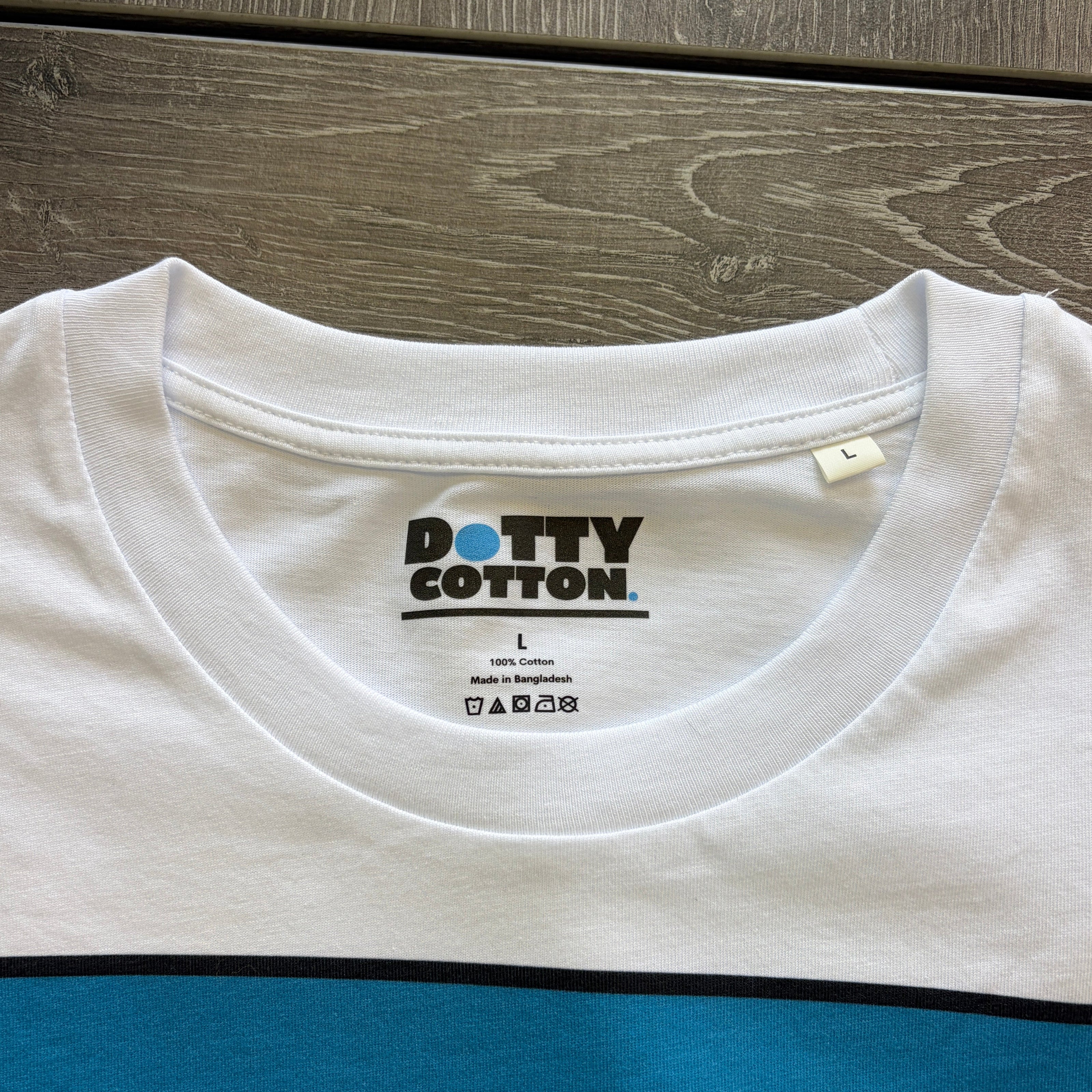 White t-shirt with blue sleeve on a wooden surface, featuring 'Dotty Cotton' branding.